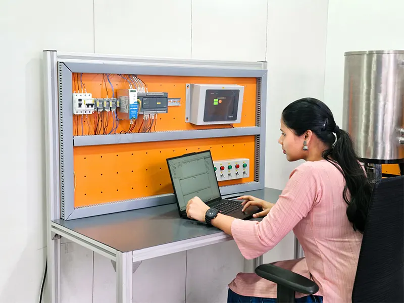 A student is seated at a workstation, working on PLC programming using a laptop. The setup includes a PLC panel with relays, an HMI screen, and control buttons, indicating a hands-on industrial automation training session.