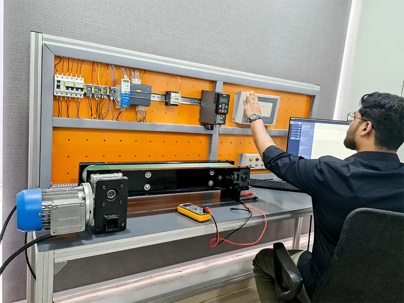 A student is working on a PLC-based automation setup. He is interacting with an HMI screen while monitoring a conveyor system controlled by a PLC.