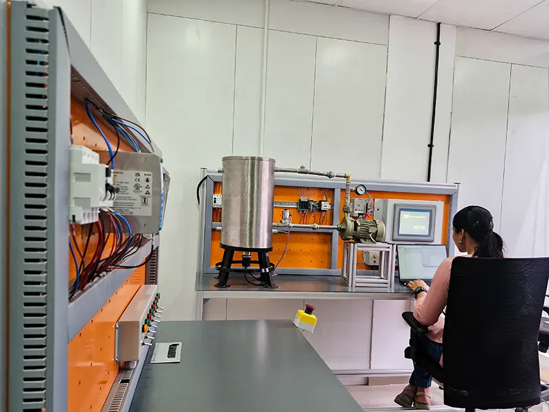 A student working on a PLC-SCADA training setup, monitoring an industrial automation system with a control panel, wiring, and an HMI screen.